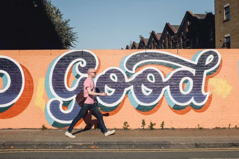 Man walking in front of "GOOD" graffiti 